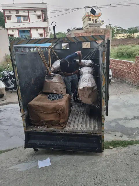 Moving crew securing wrapped household furniture with ropes inside a truck